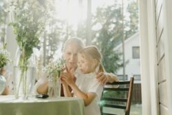 Older woman and young child sitting at table while observing a vase of flowers