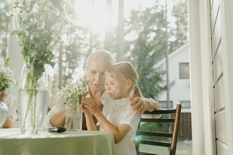 Older woman and young child sitting at table while observing a vase of flowers