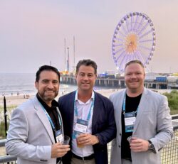 George Naveda, Aaron Metaj, and Curtis Taylor of Lima One Capital at NPLA Atlantic City conference smiling while standing in front of a boardwalk and Ferris wheel.
