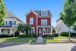 Street view of a 2-story red home with white trim in neighborhood
