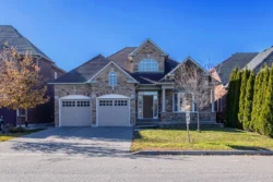 Streetview of a 2-story brick home with a 2-car garage and trees on either side
